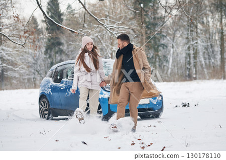 Front view, having fun. Happy couple having a walk in winter forest. Blue car is parked Front view, having fun. Happy couple having a walk in winter forest. Blue car is parked 130178110
