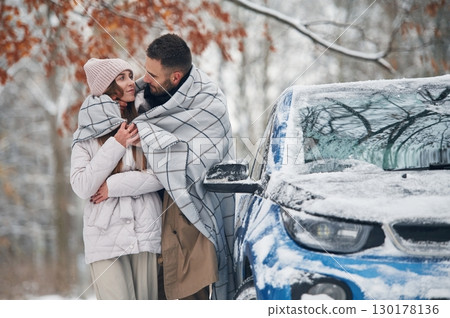 Warming by towel. Happy couple having a walk in winter forest. Blue car is parked 130178136