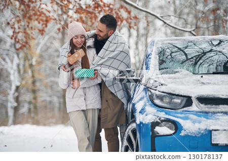 Warming by towel. Happy couple having a walk in winter forest. Blue car is parked 130178137