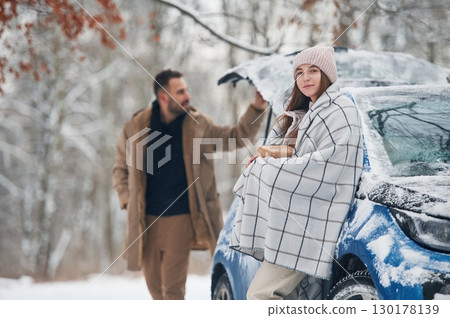 Man is holding the towel to warm the woman. Happy couple having a walk in winter forest. Blue car is parked Man is holding the towel to warm the woman. Happy couple having a walk in winter forest. Blue car is parked 130178139