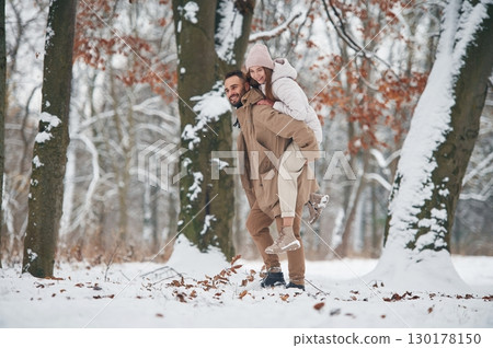 Woman is riding on the man. Lovely couple have a walk in the winter forest 130178150