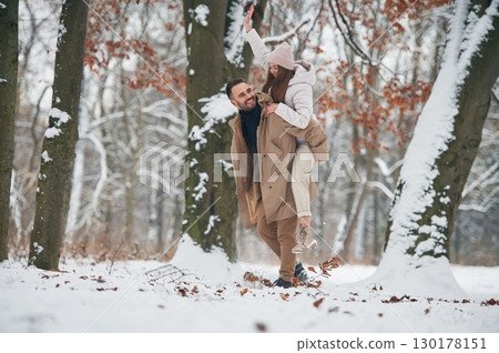Woman is riding on the man. Lovely couple have a walk in the winter forest 130178151