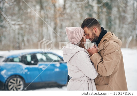 Happy couple having a walk in winter forest. Blue car is parked 130178162