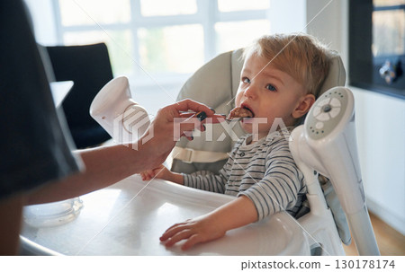 Cute baby boy is sitting and feeding by spoon by mother 130178174