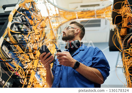 View from below. Young man is working with internet equipment and wires in server room 130178324