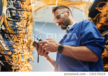 Professional device in hands. Young man is working with internet equipment and wires in server room 130178329