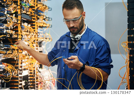 Modern technology routing. Young man is working with internet equipment and wires in server room Modern technology routing. Young man is working with internet equipment and wires in server room 130178347