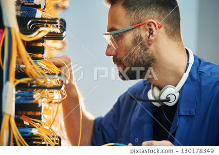 Administrator is busy. Young man is working with internet equipment and wires in server room 130178349