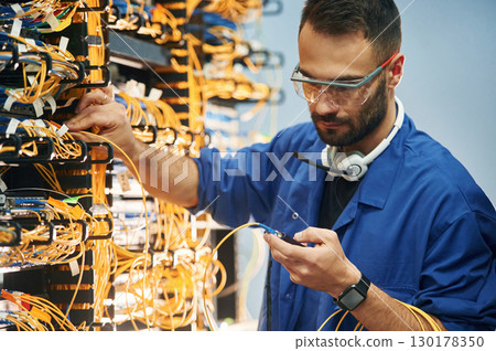 Checking signal by device. Young man is working with internet equipment and wires in server room 130178350