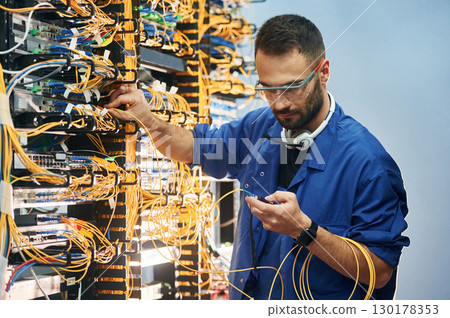 Checking signal by device. Young man is working with internet equipment and wires in server room 130178353