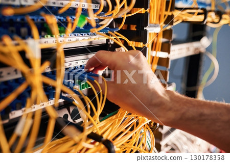 Close up view of hand that fixing internet. Young man is working with equipment and wires in server room 130178358