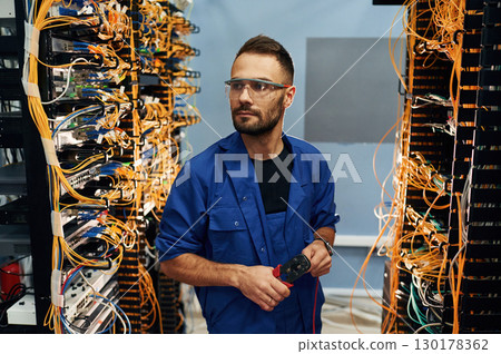 Administrator is busy. Young man is working with internet equipment and wires in server room 130178362