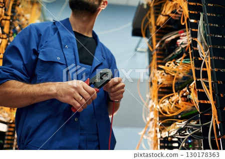 Repairman is busy and working with internet equipment and wires in server room 130178363