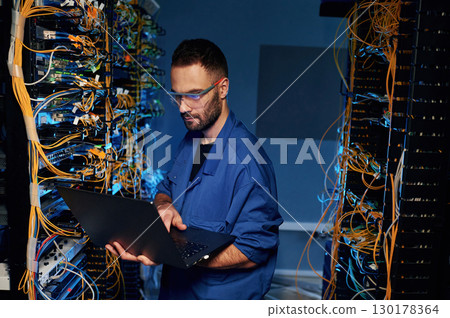 Repairman is busy and working with internet equipment and wires in server room 130178364