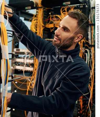 Black clothes. Young man is working with internet equipment and wires in server room Black clothes. Young man is working with internet equipment and wires in server room 130178373