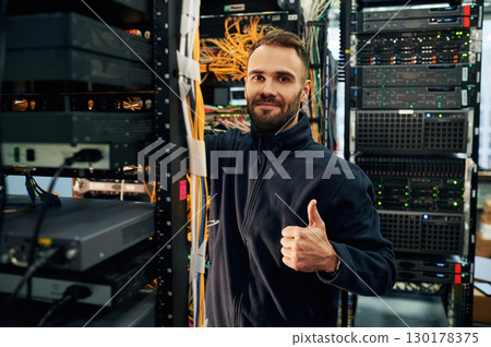 Black clothes. Young man is working with internet equipment and wires in server room Black clothes. Young man is working with internet equipment and wires in server room 130178375