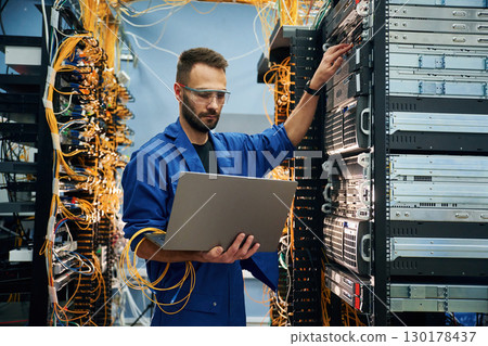 Using the laptop. Young man is working with internet equipment and wires in server room Using the laptop. Young man is working with internet equipment and wires in server room 130178437