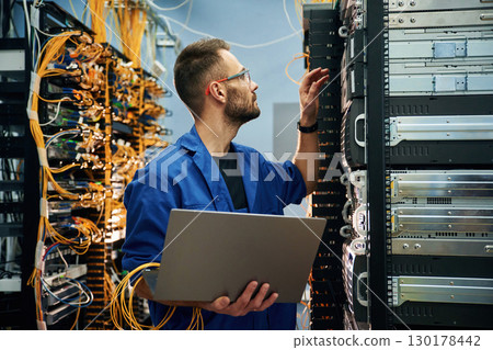 Young man is working with internet equipment and wires in server room 130178442