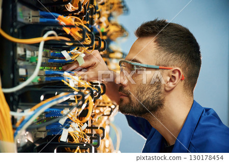 Looking extremely close at cables. Young man is working with internet equipment and wires in server room Looking extremely close at cables. Young man is working with internet equipment and wires in server room 130178454