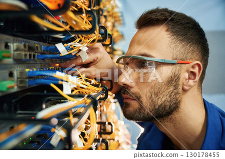 Looking extremely close at cables. Young man is working with internet equipment and wires in server room 130178455
