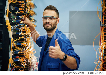 Fixed, with thumbs up. Young man is working with internet equipment and wires in server room Fixed, with thumbs up. Young man is working with internet equipment and wires in server room 130178458