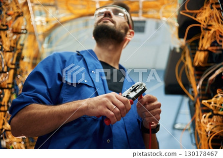 Busy by cutting the wire. Young man is working with internet equipment in server room Busy by cutting the wire. Young man is working with internet equipment in server room 130178467