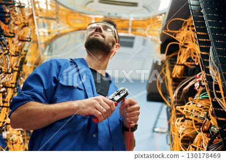Busy by cutting the wire. Young man is working with internet equipment in server room 130178469