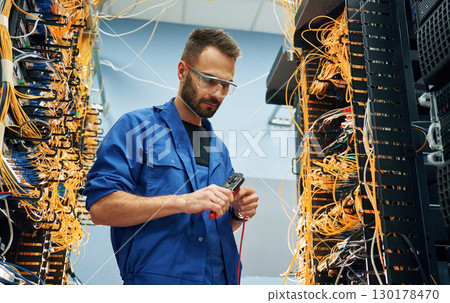 Busy by cutting the wire. Young man is working with internet equipment in server room Busy by cutting the wire. Young man is working with internet equipment in server room 130178470