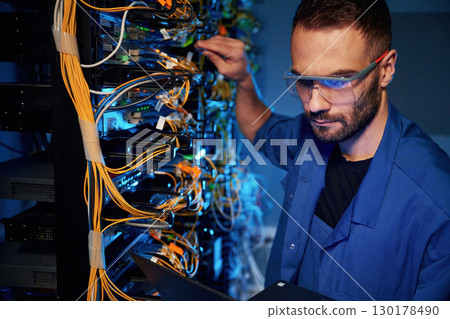 In glasses. Young man is working with internet equipment and wires in server room 130178490