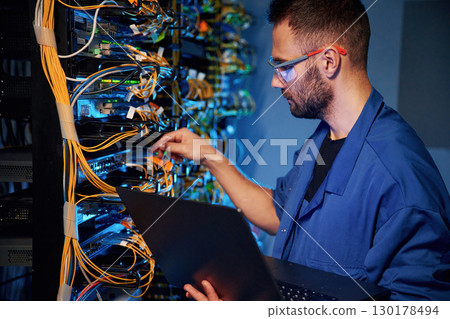 Cables management. Young man is working with internet equipment and wires in server room Cables management. Young man is working with internet equipment and wires in server room 130178494