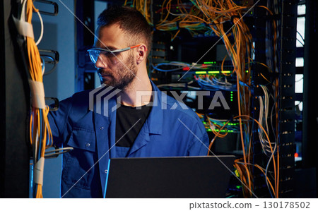 Blue colored lighting. Young man is working with internet equipment and wires in server room Blue colored lighting. Young man is working with internet equipment and wires in server room 130178502
