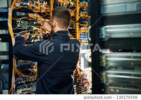 Young man is working with internet equipment and wires in server room Young man is working with internet equipment and wires in server room 130178506