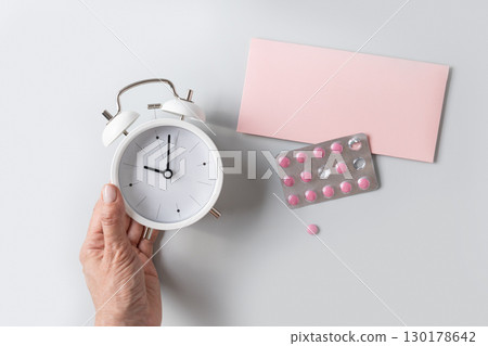 Concept of sleep problems. Woman hand with alarm clock and pills 130178642
