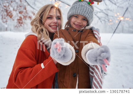 Holding sparklers, new year. Mother and her daughter is on the winter meadow and forest 130178741
