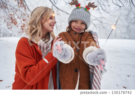 Holding sparklers, new year. Mother and her daughter is on the winter meadow and forest 130178742