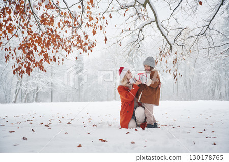 In Santa clothes, with gift box. Mother and her daughter is on the winter meadow and forest In Santa clothes, with gift box. Mother and her daughter is on the winter meadow and forest 130178765