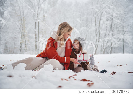 Joy, sitting on the snow. Mother and her daughter is on the winter meadow and forest 130178782