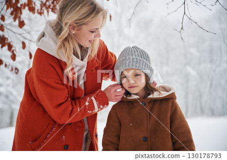 Wearing the hat to the girl. Mother and her daughter is on the winter meadow and forest Wearing the hat to the girl. Mother and her daughter is on the winter meadow and forest 130178793