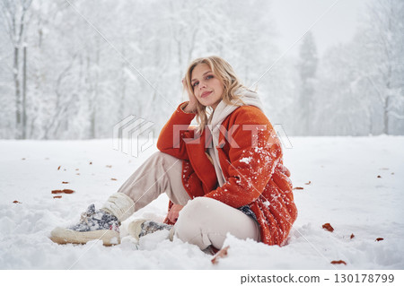 Beautiful woman in red warm jacket is sitting on the winter field Beautiful woman in red warm jacket is sitting on the winter field 130178799