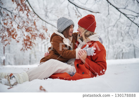 Sitting on the ground. Mother and her daughter is on the winter meadow and forest Sitting on the ground. Mother and her daughter is on the winter meadow and forest 130178888