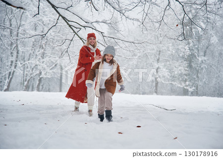 Running forward. Mother and her daughter is on the winter meadow and forest Running forward. Mother and her daughter is on the winter meadow and forest 130178916
