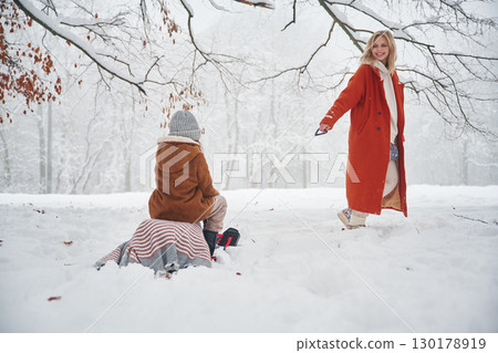 Riding on the sled. Mother and her daughter is on the winter meadow and forest 130178919