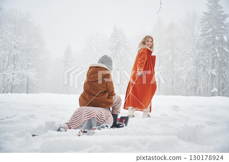 Sled ride. Mother and her daughter is on the winter meadow and forest Sled ride. Mother and her daughter is on the winter meadow and forest 130178924