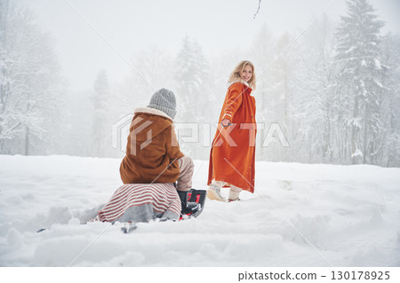 Sled ride. Mother and her daughter is on the winter meadow and forest Sled ride. Mother and her daughter is on the winter meadow and forest 130178925