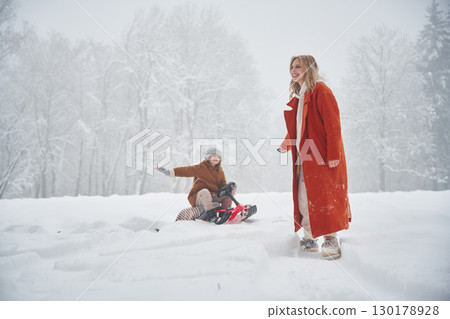A woman pulls a sled. Mother and her daughter is on the winter meadow and forest 130178928