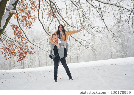 Holding woman that rides him. Beautiful couple are standing together on the snowy field of forest 130178999