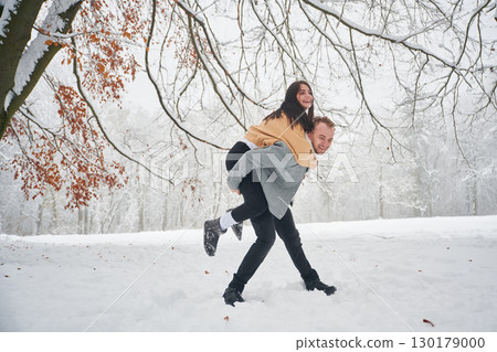 Holding woman that rides him. Beautiful couple are standing together on the snowy field of forest 130179000