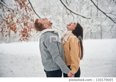 Standing and enjoying snow. Beautiful couple are together on the field of forest 130179005