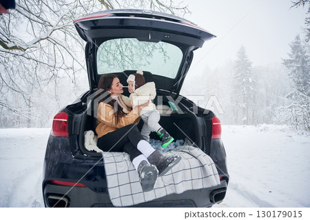 Mother and son on the trunk of car, sitting. Outdoors, winter field Mother and son on the trunk of car, sitting. Outdoors, winter field 130179015