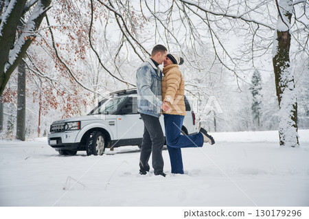 Conception of love. Beautiful couple standing near the car in the winter forest Conception of love. Beautiful couple standing near the car in the winter forest 130179296